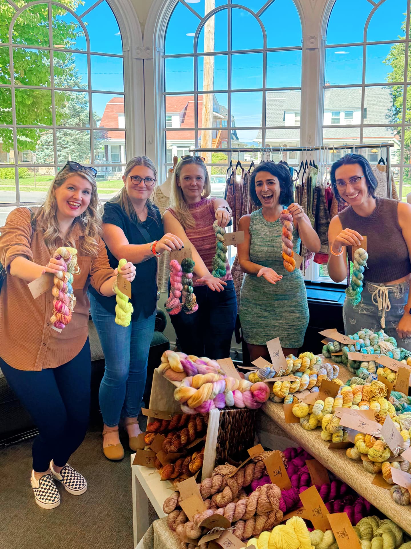 Coven members holding up skeins of hand-dyed yarn at a local yarn shop