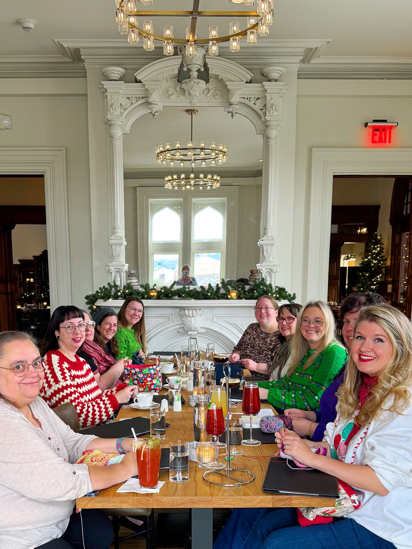 Coven members gathered around a long table at a holiday brunch with knitting projects